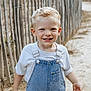 child, boy, blonde_hair, blue_eyes, denim_overalls, white_tshirt, smiling, outdoor, fence, sand, path, portrait, happy, casual_clothing, daylight, nature, person, cute, young_child, summer