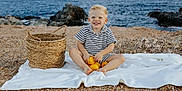 Giovanni participe au concours pour gagner de l'argent avec cette photo : toddler, child, smiling, blonde_hair, striped_clothing, lemons, basket, beach, rocky_shore, blanket, sea, outdoor, happy, sitting, nature, coast, summer, vacation, playful, sunlight