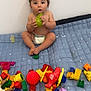 toddler, child, pear, toy, colorful_toys, quilt, blue_quilt, diaper, indoor, playtime, curious, sitting, bare_chest, soft_lighting, cute, expression, face, hands, feet, playroom