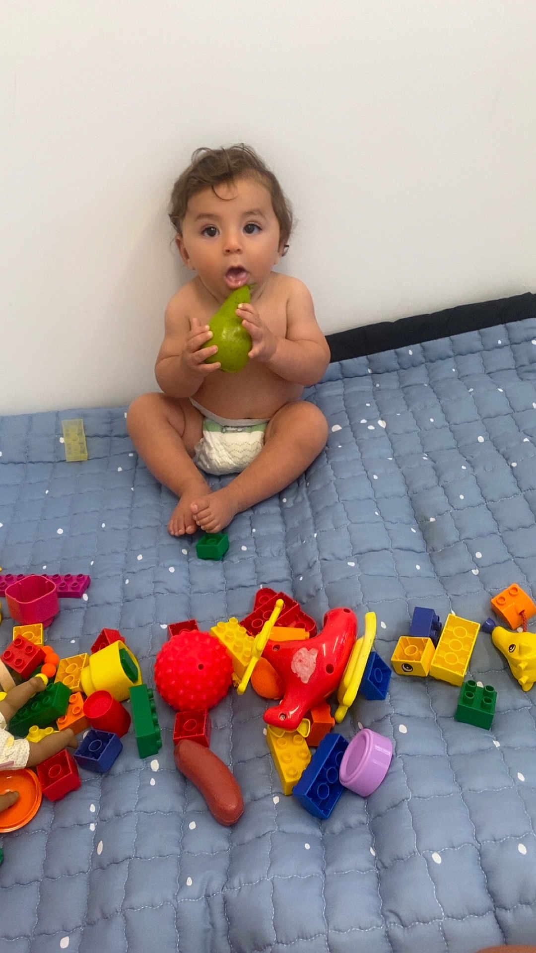 Imran participe au concours pour gagner de l'argent avec cette photo : toddler, child, pear, toy, colorful_toys, quilt, blue_quilt, diaper, indoor, playtime, curious, sitting, bare_chest, soft_lighting, cute, expression, face, hands, feet, playroom
