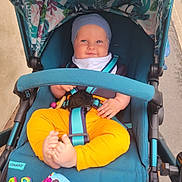 Dominic is registered to the contest to win money with this photo: baby, stroller, blue_hat, yellow_pants, smiling, baby_toy, straps, feet, hand, outdoor, person, child, seat, fabric, colorful, happy, cute, infant, casual_clothing, cosatto