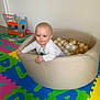 baby, ball_pit, balls, child, colorful, floor, foam_mat, happy, indoor, infant, padded_mat, play_area, playtime, room, smiling, soft_toys, toy_cart, white_clothing, wooden_toy, young_child