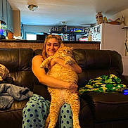 Thumbs is registered to the contest to win money with this photo: blanket, cat, ceiling, couch, cozy, food_items, game_controller, happy, hugging, indoor, kitchen, lamp, leather_couch, orange_cat, pajama_pants, person, polka_dots, refrigerator, shelf, smiling