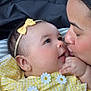 baby, infant, parent, kiss, closeup, yellow_dress, headband, bow, gingham, flower_applique, earring, hand, eyes, smile, car_seat, seat_headrest, skin, affection, family, portrait