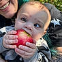 Leanne is registered to the contest to win money with this photo: apple, baby, camo_sweater, chewing, child, closeup, daylight, eyes, face, green_hair, hand, happy, holding, nature, outdoor, person, portrait, skin, smiling_adult, tattoos