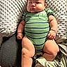 baby, infant, child, portrait, lying_down, onesie, green_clothing, striped_clothing, pillow, blanket, bed, indoor, face, eyes, hands, legs, cozy, serious_expression, close_up, photography