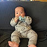 baby, infant, child, sitting, couch, sofa, teething_toy, toy, smiling, face, portrait, indoors, living_room, clothing, onesie, barefoot, feet, furniture, home, photography
