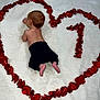 baby, infant, rose_petals, heart_shape, number_one, white_blanket, black_pants, bare_skin, lying_down, celebration, milestone, soft_texture, top_view, cute, newborn, love, toddler, skin, peaceful, resting