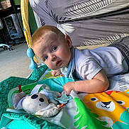 Jaxson joined the competition — help win amazing prizes! baby, infant, play_mat, toy, plush, koala, pacifier, floor, carpet, chair, blue_eyes, white_shirt, gray_pants, indoor, child, curious, colorful, animal_print, person, crawling