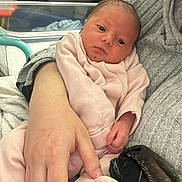 Arabella is registered to the contest to win money with this photo: newborn, baby, infant, person, hand, pink_clothing, hospital, cradle, blanket, adult, skin, face, curly_hair, bed, medical_equipment, cozy, soft, comfort, indoor, care