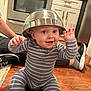 baby, child, striped_onesie, metal_bowl, hat, smiling, happy, floor, kitchen, wooden_floor, adult_legs, sneakers, cup, brush, home, indoor, playful, person, cooking_tools, cute