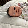 Ember is registered to the contest to win money with this photo: baby, infant, face, eyes, smile, onesie, patterned_clothing, blanket, bed, soft, cute, child, lying_down, portrait, closeup, skin, head, happy, newborn, indoors