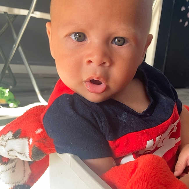 Elijah joined the competition — help win amazing prizes! baby, blanket, box, child, curious, cute, expression, face, floor, furniture, head, indoor, infant, light, person, red, shirt, sitting, skin, young