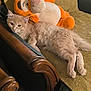 cat, plush_toy, couch, furniture, indoor, pet, animal, relaxing, beige_cat, soft, cozy, stuffed_animal, tiger_toy, wooden_armrest, fabric, home, resting, cute, fluffy, living_room