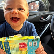 Adrian joined the competition — help win amazing prizes! baby, child, infant, smiling, happy, laughing, portrait, face, car, car_interior, car_seat, book, activity_book, dinosaur, reading, outdoor, city, sunlight, blue_shirt, joy