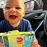 baby, child, infant, smiling, happy, laughing, portrait, face, car, car_interior, car_seat, book, activity_book, dinosaur, reading, outdoor, city, sunlight, blue_shirt, joy