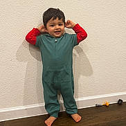 Shajun is registered to the contest to win money with this photo: toddler, child, onesie, green_clothing, red_sleeves, barefoot, standing, white_wall, wooden_floor, toys, playful, smiling, happy, indoor, person, young_child, cute, casual_clothing, home, portrait