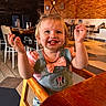 celebration, child, clothing, cute, denim_overall, expression, face, hair, happy, high_chair, indoor, messy_hair, mickey_mouse_patch, person, pink_shirt, restaurant, smiling, table, toddler, wooden_chair
