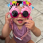 Camila is registered to the contest to win money with this photo: toddler, child, birthday, sunglasses, cupcake, pink, purple_clothing, happy, smile, celebration, indoors, floor, playful, face, person, cute, fun, party_accessory, glasses, baby
