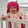Camila is registered to the contest to win money with this photo: baby, crib, toddler, smiling, red_towel, ladybug, indoors, child, happy, infant, white_crib, person, cute, blanket, playful, headwear, clothing, window_blinds, soft_light, standing