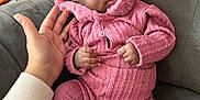 Laila is registered to the contest to win money with this photo: baby, child, pink_outfit, hood, knitted_clothing, hand, couch, seated, indoor, cozy, cute, footwear, soft_texture, portrait, infant, warm_clothing, person, fingers, comfortable, closeup
