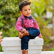Diyan joined the competition — help win amazing prizes! child, boy, outdoor, sitting, red_shirt, bow_tie, suspenders, brown_boots, casual_pose, green_background, young, cute, fashion, portrait, smiling, crossed_legs, stone_ledge, short_hair, daylight, nature