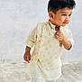 Diyan is registered to the contest to win money with this photo: child, boy, traditional_clothing, cream_outfit, brown_shoes, standing, outdoor, portrait, young_child, curly_hair, walking, concrete_floor, white_wall, smiling, cute, fashion, person, small_boy, casual_pose, happy