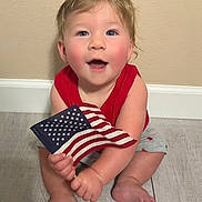 Tyler joined the competition — help win amazing prizes! baby, child, flag, american_flag, red_shirt, gray_shorts, sitting, floor, wooden_floor, smiling, happy, blue_eyes, rosy_cheeks, indoor, person, one_person, cute, patriotic, young_child, caucasian