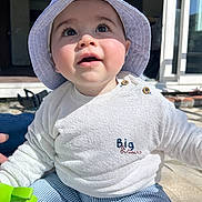 Achille a rejoint le concours — aidez-le/la à gagner de superbes lots ! baby, infant, bucket_hat, striped_hat, blue_and_white, big_eyes, long_eyelashes, white_sweater, striped_pants, green_toy, sitting, outdoor, sunlight, portrait, cheeks, cute, buttons, patio, window, candid
