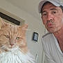 man, cat, indoor, selfie, white_cap, fluffy_cat, orange_cat, white_shirt, wall_light, door, window, facial_expression, pouting, pet, animal, feline, portrait, closeup, human, casual