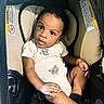 automobile, baby, blue_socks, car_seat, child, curious, emojis, eyes, face, indoors, infant, looking_at_camera, padded_seat, photograph, portrait, safety_harness, short_hair, sitting, vehicle, white_onesie