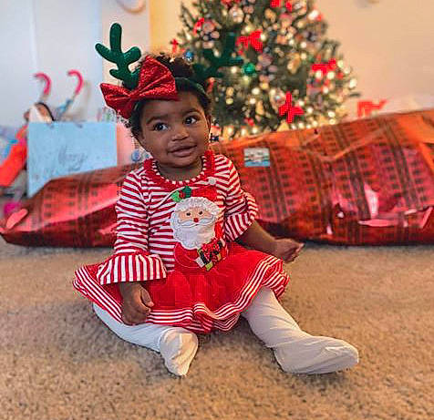 Marley is registered to the contest to win money with this photo: baby, child, christmas, christmas_decoration, christmas_eve, christmas_ornament, christmas_tree, event, fun, happy, head, headwear, holiday, person, plant, play, red, sitting, smile, toddler