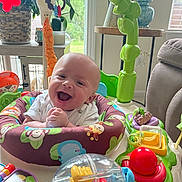 Dean is registered to the contest to win money with this photo: baby, smiling, indoor, activity_jumper, toy, colorful, happy, child, infant, face, furniture, window, plant, couch, table, light, play, room, person, cute