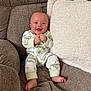 Dean is registered to the contest to win money with this photo: baby, smiling, couch, pillow, onesie, infant, happy, clothing, sitting, barefoot, indoor, cute, child, soft_fabric, plush, person, portrait, comfortable, cozy, young