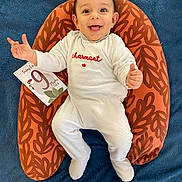 Marceau participe au concours pour gagner de l'argent avec cette photo : baby, infant, smiling, white_onesie, cushion, orange, leaf_pattern, blue_blanket, milestone_card, happy, child, portrait, indoor, cute, hands, feet, sitting, person, young_child, expression