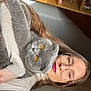 woman, cat, gray_cat, glasses, lipstick, indoor, shelf, cosy, portrait, pet, amber_eyes, long_hair, sweater, holding, furniture, personal_care_items, face, home, relaxation, casual