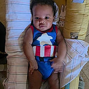 Aerrrow is registered to the contest to win money with this photo: baby, child, infant, onesie, superhero_costume, captain_america, yellow_cushion, animal_print, black_socks, face, eyes, hands, legs, person, indoor, floor, blanket, striped_cloth, cute, portrait