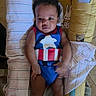 baby, child, infant, onesie, superhero_costume, captain_america, yellow_cushion, animal_print, black_socks, face, eyes, hands, legs, person, indoor, floor, blanket, striped_cloth, cute, portrait