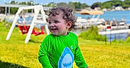 Liam Nicholas is registered to the contest to win money with this photo: boats, child, curly_hair, daytime, fun, grass, green_shirt, happy, lake, outdoor, play, shark_design, smiling, splash_pad, summer, sunny, swimsuit, swing_set, toddler, water_play