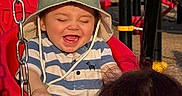 Liam Nicholas is registered to the contest to win money with this photo: toddler, child, swing, playground, hat, striped_shirt, red, happy, laughing, outdoor, sunlight, adult, chain, play_equipment, person, smile, fun, recreation, park, joy