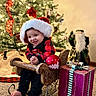 Liam Nicholas joined the competition — help win amazing prizes! baby, child, santa_hat, christmas_tree, ornaments, ribbon, wooden_sleigh, gift_box, carpet, festive_clothing, holiday_decor, smiling, indoors, decorations, santa_figurine, christmas, present, happy, tongue_out, cozy