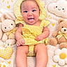 baby, infant, child, smiling, happy, portrait, yellow_outfit, gingham, bonnet, tongue_out, lying_down, teddy_bear, stuffed_animal, flowers, daisies, cloud_pillow, hearts, blanket, indoor, colorful