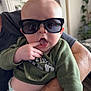 Braxton is registered to the contest to win money with this photo: baby, infant, sunglasses, hand, finger, diaper, onesie, adult_arm, smartwatch, reflection, indoor, houseplant, mirror, portrait, cute, expression, green_shirt, skin, close_up, holding