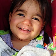 Orion participe au concours pour gagner de l'argent avec cette photo : child, toddler, smile, teeth, face, eyes, dark_hair, cheeks, car_seat, red_seat, blanket, plush, toy, rattle, hoodie, closeup, portrait, happy, candid, sunlight
