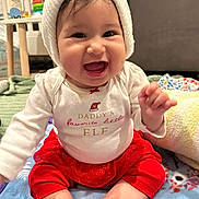 Natalia joined the competition — help win amazing prizes! baby, child, smiling, happy, sitting, hat, clothing, red_skirt, white_shirt, blanket, indoors, face, cute, infant, festive, holiday, knitted_hat, expression, person, toddler