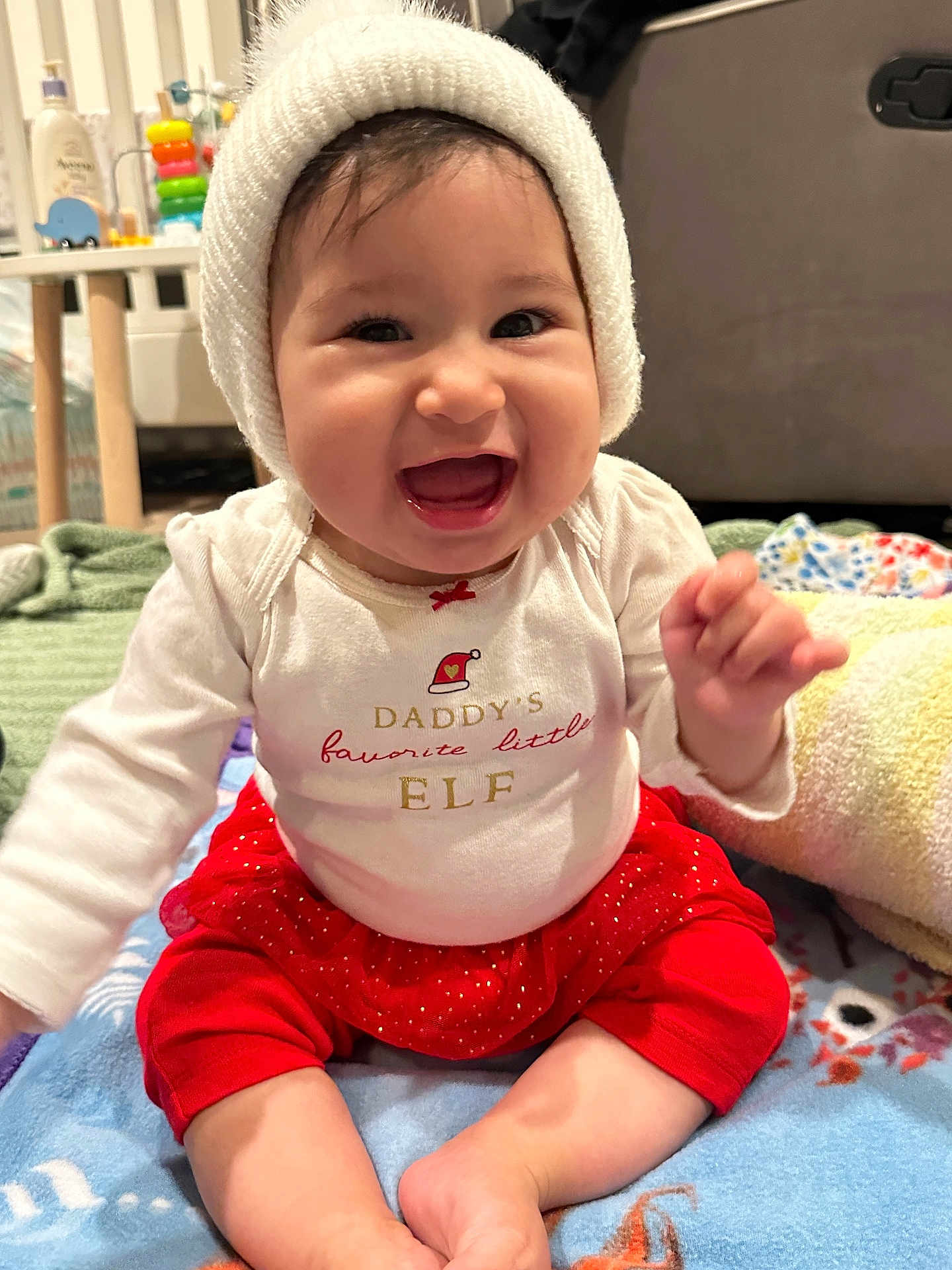 Natalia joined the competition — help win amazing prizes! baby, child, smiling, happy, sitting, hat, clothing, red_skirt, white_shirt, blanket, indoors, face, cute, infant, festive, holiday, knitted_hat, expression, person, toddler