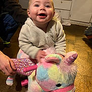 Jayda is registered to the contest to win money with this photo: baby, cabinet, child, drawer, floor, hand, happy, indoor, infant, jacket, motion_blur, pastel_colors, playing, plush_toy, portrait, smiling, sparkle, stuffed_animal, toy_handle, unicorn_toy