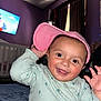 toddler, child, smiling, pink_cap, light_green_sweater, indoor, bedroom, crib, television, cartoon, purple_wall, curtains, happy, baby, person, face, hand, expression, cute, playful