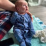 baby, infant, blue_onesie, dinosaur_pattern, blanket, hand, plaid, smartphone, floor, curtain, window, indoors, clothing, footed_pajamas, expression, looking_up, cute, soft_texture, child, person