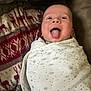 baby, infant, face, tongue, swaddle, blanket, pattern, stars, moon, reindeer, red, beige, cozy, happy, playful, cute, indoor, person, portrait, smile